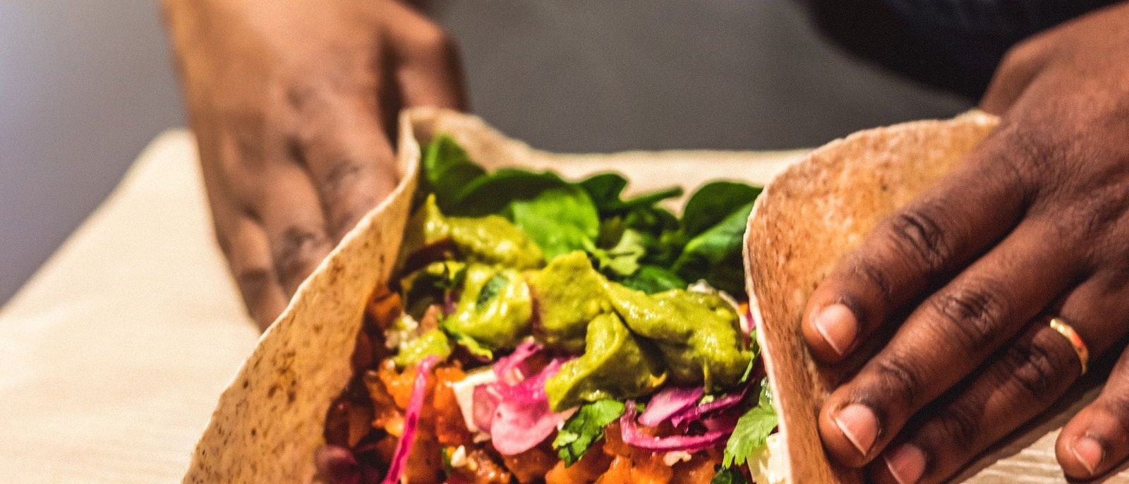Burrito Bala a ser enrolado à mão, com guacamole, espinafres e cebola roxa